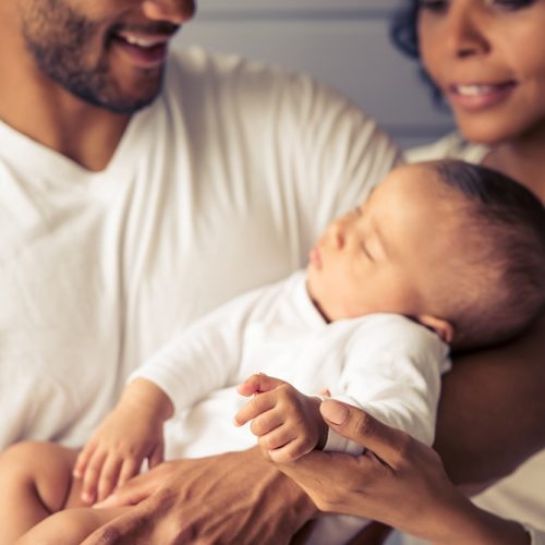 Cropped image of beautiful young Afro American parents smiling while little baby is sleeping in dad's arms